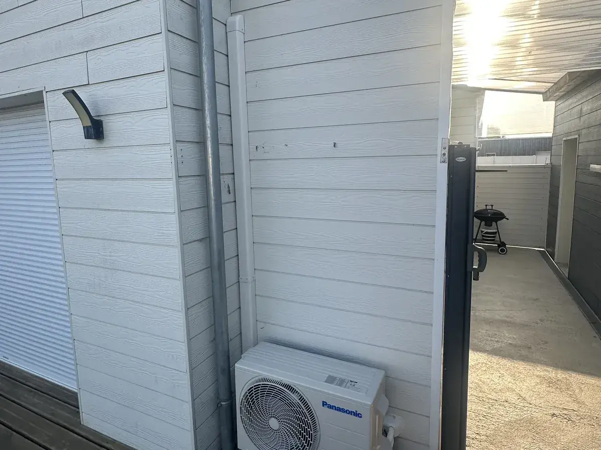 Unité extérieure de climatisation réversible posée sur plots au pied d’une façade de pavillon en Sarthe