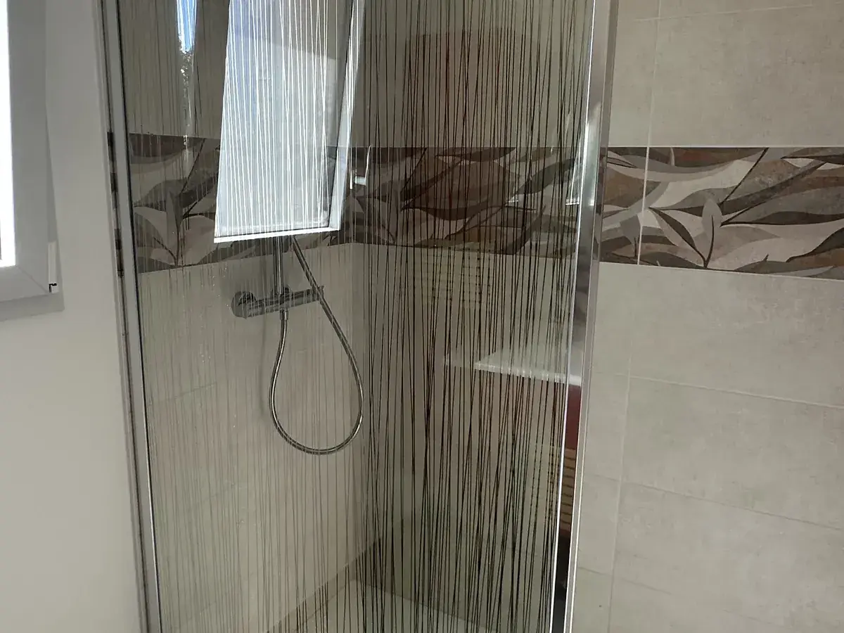 Douche à l’italienne avec receveur extra-plat, paroi de verre fixe et faïence claire dans une salle de bain neuve en Sarthe