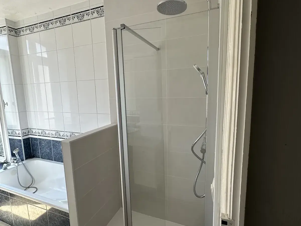 Douche avec receveur extra-plat, paroi de verre et colonne thermostatique créée à côté d’une baignoire conservée