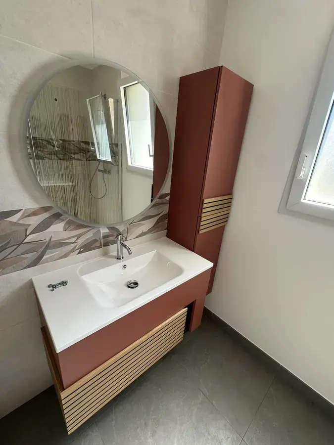 Meuble vasque suspendu terracotta et miroir rond rétroéclairé dans une salle de bain neuve en Sarthe