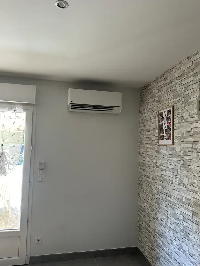 Séjour avec mur en parement pierre et unité de climatisation murale au-dessus de la baie vitrée
